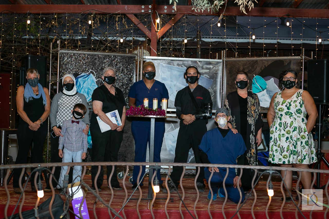 A group of people--all wearing masks, some in scrubs--standing in front of a backdrop of large photos of discarded face masks